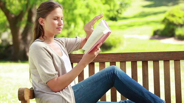 一个女人坐在长凳上看小说视频素材