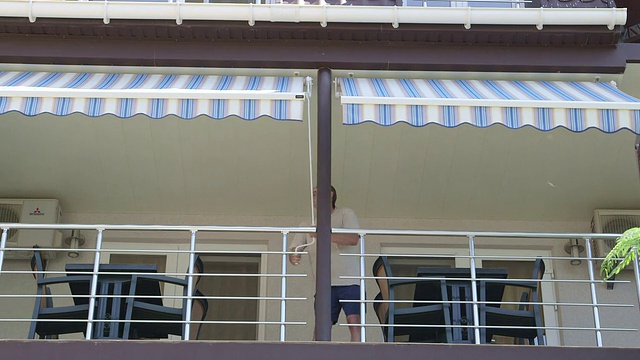 一名男子在酒店露台前展开可伸缩遮阳篷视频下载