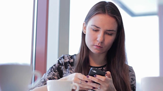 拿着智能手机在咖啡馆喝拿铁咖啡的女人视频下载