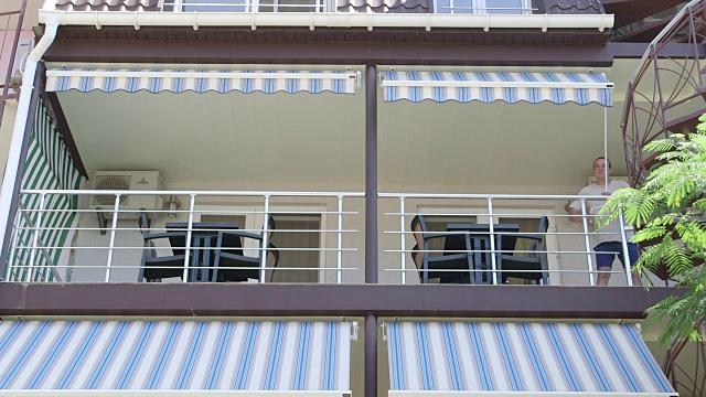夏日酒店的遮阳阳台在一个阳光明媚的日子展开伸缩遮阳蓬视频下载