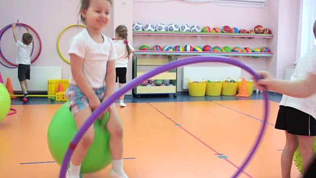 在幼儿园里，小女孩和其他孩子一起在绿色的球上跳视频素材