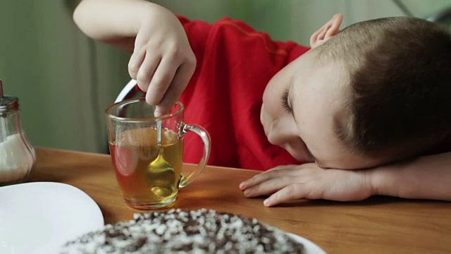 穿红衬衫的小男孩正在用勺子往茶里加糖。视频下载