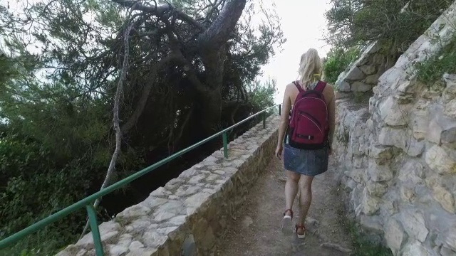 女游客在春季到地中海国家旅游。女孩走在以大海为背景的石路上视频下载