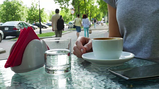 在咖啡馆喝咖啡的女人。玻璃杯在杯子旁边视频素材