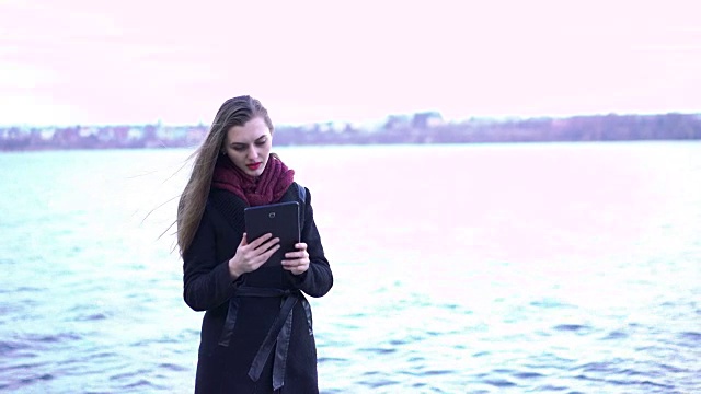 年轻美丽的女子在湖边使用平板电脑视频下载