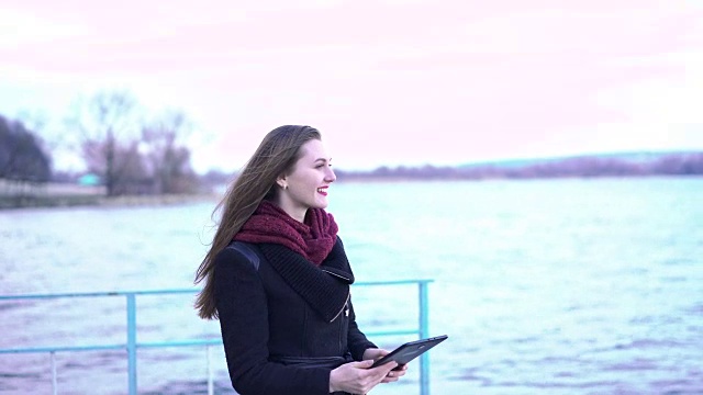 年轻美丽的女子在湖边使用平板电脑。FullHD视频素材