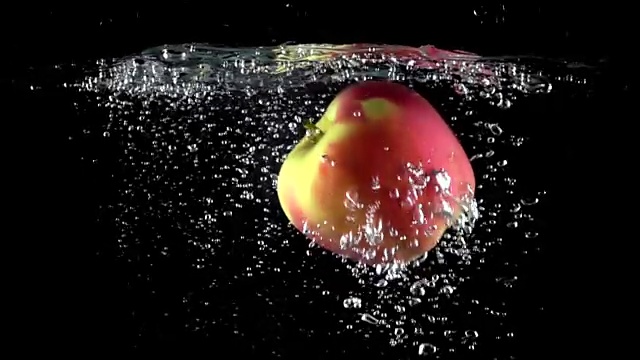 近距离拍摄的苹果落在水与黑色的背景。超级慢动作视频下载