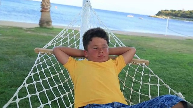小男孩在海边的吊床上休息视频下载