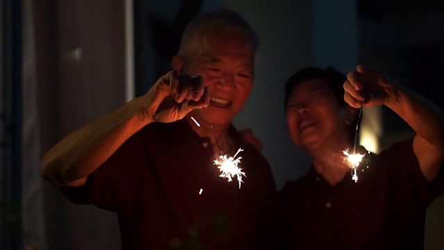 亚洲老夫妇玩烟花，烟花，爆竹在晚上。庆祝生活的概念视频下载