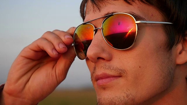 帅气的年轻时尚男子戴着太阳镜，看起来日落在野外视频下载