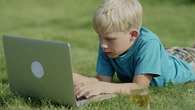 男孩在草地上用笔记本电脑视频下载