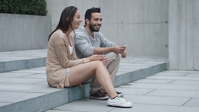 年轻的快乐微笑的男人和女人正坐在户外的台阶上交流。视频下载