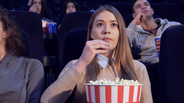 在电影院，女孩慢慢地把爆米花放进嘴里视频素材