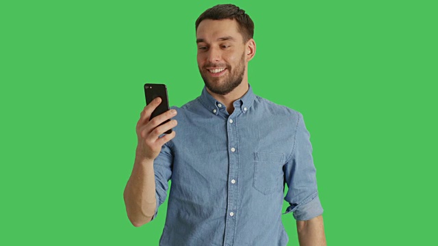 中景的一个时尚的男人做视频电话和显示/指向他身后的景点。拍摄在绿色屏幕背景。视频下载