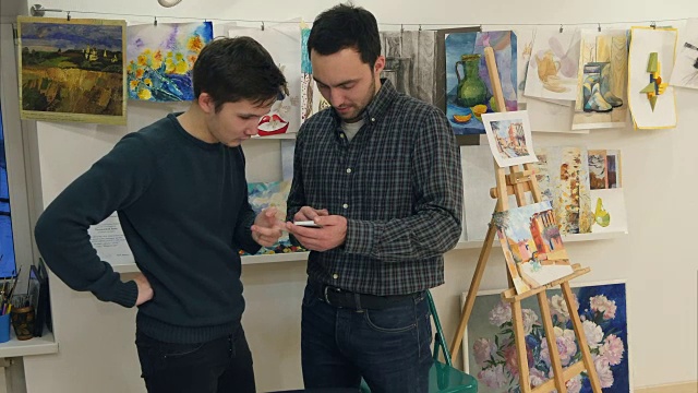 两个年轻人在美术课上用智能手机视频下载