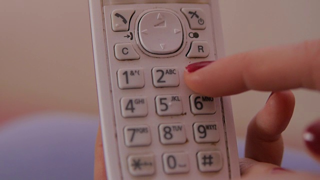 女性用红指甲握着座机，拨着电话号码。视频素材