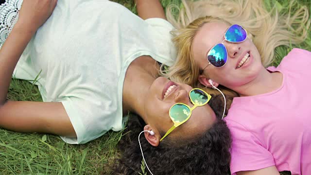 两个美丽的女孩躺在草地上，听着音乐，一起唱歌视频下载
