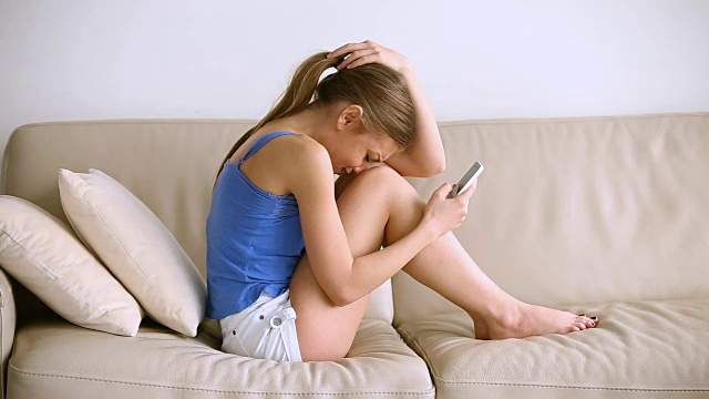 悲伤的少女坐在沙发上看手机哭视频素材