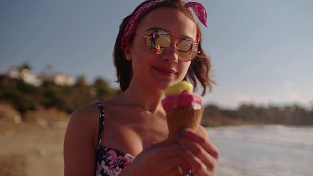 年轻时髦的女人一边吃冰淇淋一边在海滩上散步视频下载
