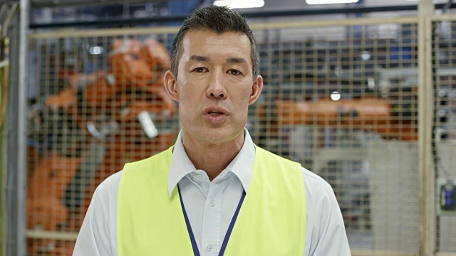 一名男性工程师在与工厂的视频通话中，背景中是正在操作的工业机器人视频下载