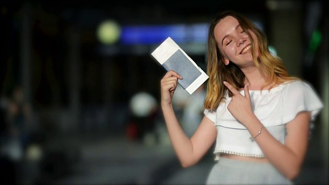 快乐微笑的少女在机场用手指展示她的护照和机票。背景上模糊的记分牌视频下载