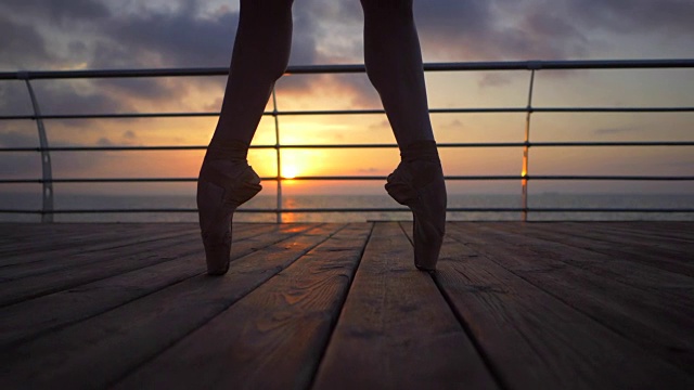 一个芭蕾舞者的脚的特写，因为她练习脚尖练习在海堤附近或海洋，日出的背景，剪影的女人的脚在尖头鞋。芭蕾舞女演员表演经典芭蕾舞剧。慢动作视频下载