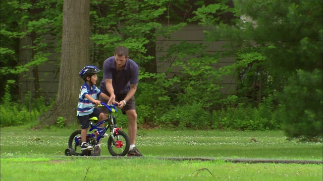 在新泽西州范伍德的一个公园里，一个男孩在学习骑自行车时，一个男人在他旁边跑步视频素材
