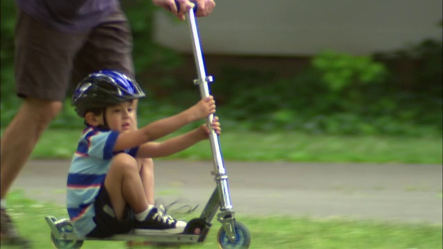 新泽西州范伍德，一名男子在公园里推着滑板车，一个男孩坐在上面视频素材