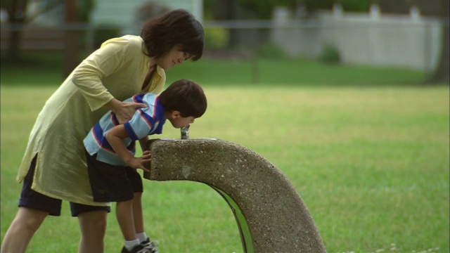 母亲抱着儿子，让他在新泽西州公园/范伍德的喷泉里喝水视频素材