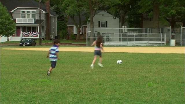 新泽西，Fanwood，男子从男孩手中抢过足球并扔出去/女孩和男孩在棒球场上追着球跑视频素材