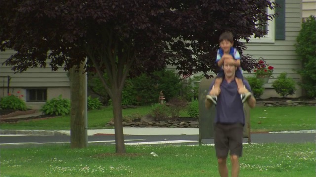 MS Man抱起一个男孩，把男孩放在他的肩膀上，带着他在郊区公园/ Fanwood，新泽西州视频素材