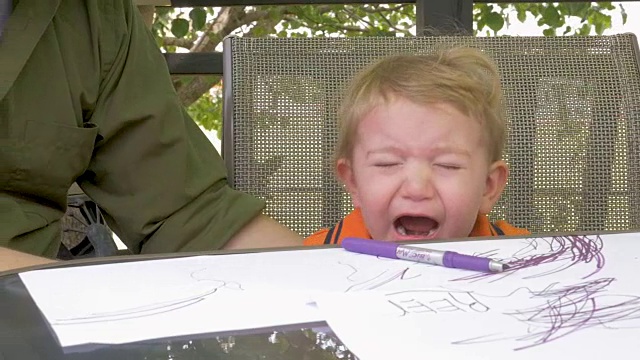 一个疲惫哭泣的小孩坐在桌子旁上色视频素材