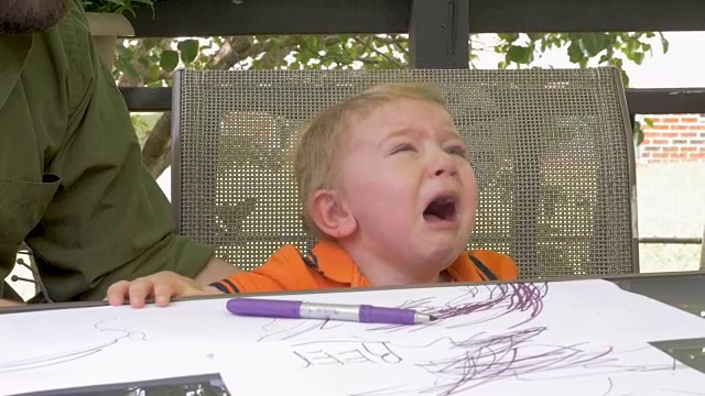 在慢镜头中，一位父亲将一个记号笔递给正在哭泣的沮丧的小男孩视频素材