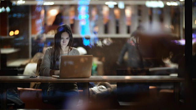 在晚上使用笔记本电脑的漂亮女人的窗口内的视图。女士关上电脑，离开咖啡厅视频下载