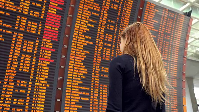 一个女人在机场看飞机航班信息板视频素材