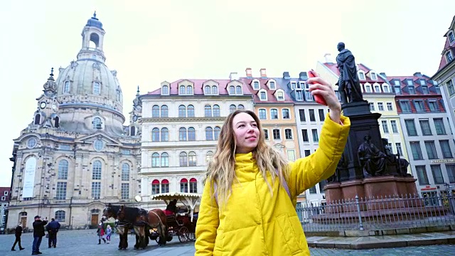 美丽的女孩通过电话打电话，在网上显示欧洲老城德累斯顿在冬天的一天在大街上的景象视频下载