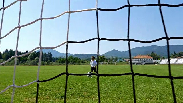 一个3岁小男孩在足球场上进球的跟踪摄像机视频下载