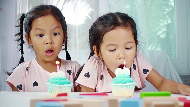 两个亚洲小女孩在家里一起吹灭生日蛋糕上的蜡烛。慢动作拍摄在工作室。视频下载