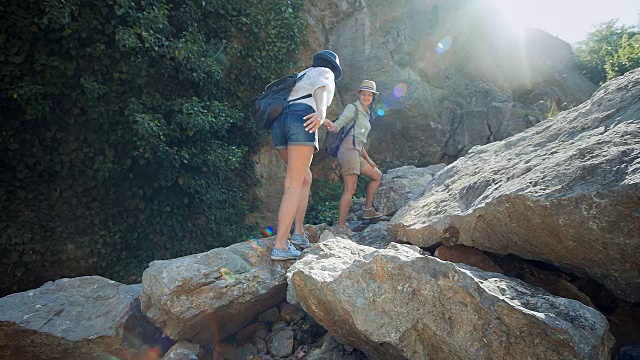 一个女旅行者在帮助她的朋友爬岩石。视频下载