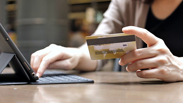 手里拿着信用卡的女人用平板电脑在网上购物，慢镜头视频购买