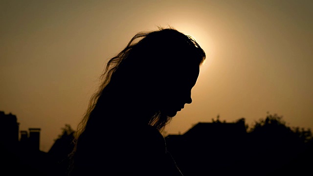 年轻苗条的女子，长波浪的头发是走在傍晚的乡村，近距离肖像背对着太阳视频下载