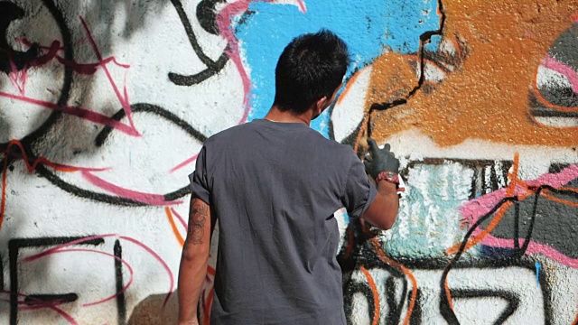 英俊的天才小男孩用喷雾剂在城市的街道墙上涂鸦。电影色调的慢动作镜头。创造性的艺术视频下载
