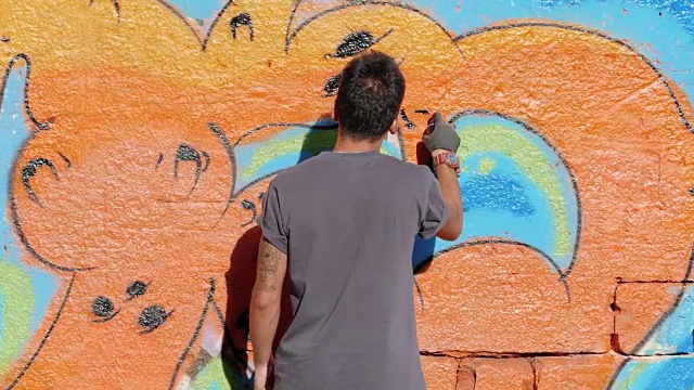 英俊的天才小男孩用喷雾剂在城市的街道墙上涂鸦。电影色调的慢动作镜头。创造性的艺术。后视图，总体规划视频下载