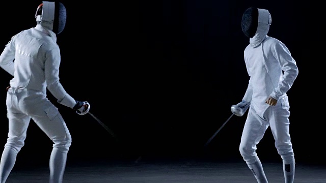 两位职业击剑选手在花剑比赛中展示了高超的剑术。他们跳跃、冲刺和弓步。拍摄孤立的黑色背景。视频素材