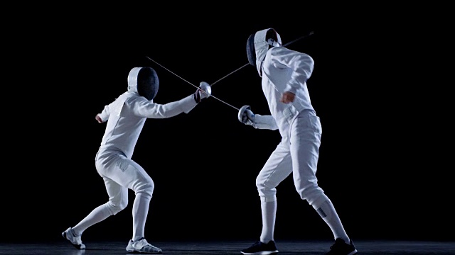 两名装备齐全的职业击剑手熟练地用剑剑格斗。他们攻击，防御，跳跃，刺和弓步。拍摄在慢动作和孤立的黑色背景。视频素材