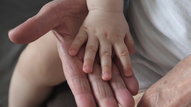 布满皱纹的老手抚摸着婴儿柔软的手。视频下载