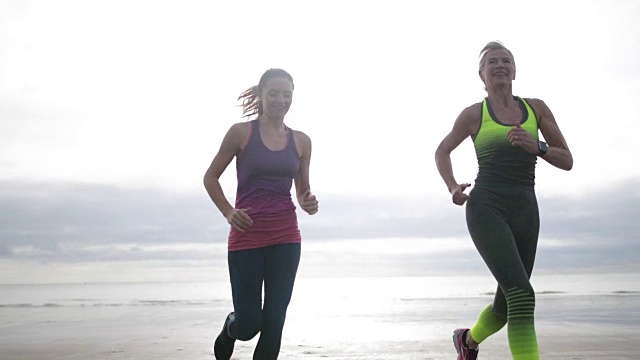 活跃的老年妇女和女儿在海滩上跑步视频素材