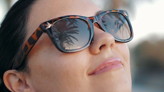 Cinemagraph -美丽的年轻的黑发微笑女孩在复古太阳镜在热带度假。棕榈树反射在玻璃上。旅行的概念。慢动作视频下载