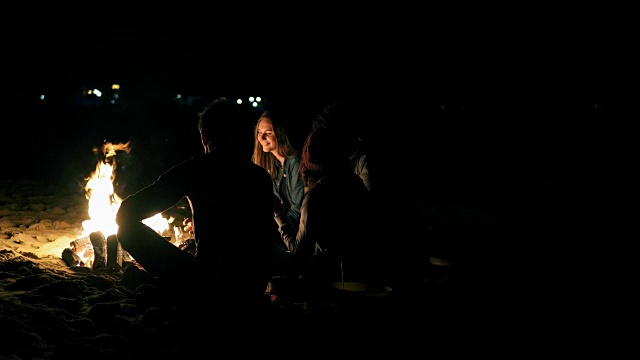 后视图的年轻人不同的人坐在一起坐在火深夜。愉快的朋友在一起聊天，一起喝啤酒视频素材