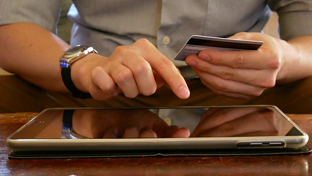 手持信用卡、使用平板电脑触摸屏进行网上购物的男子——特写视频素材